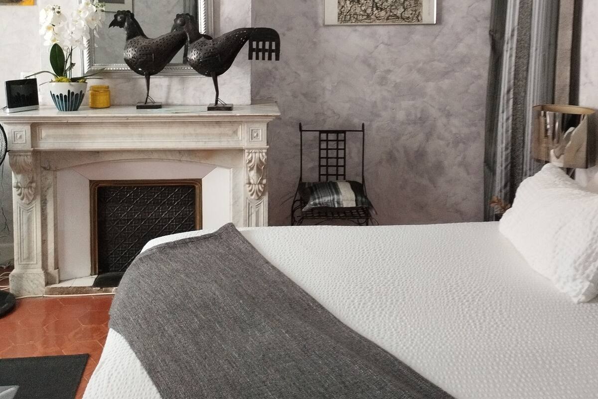 A bedroom with a large bed, a fireplace, a mirror, and a painting on the wall.