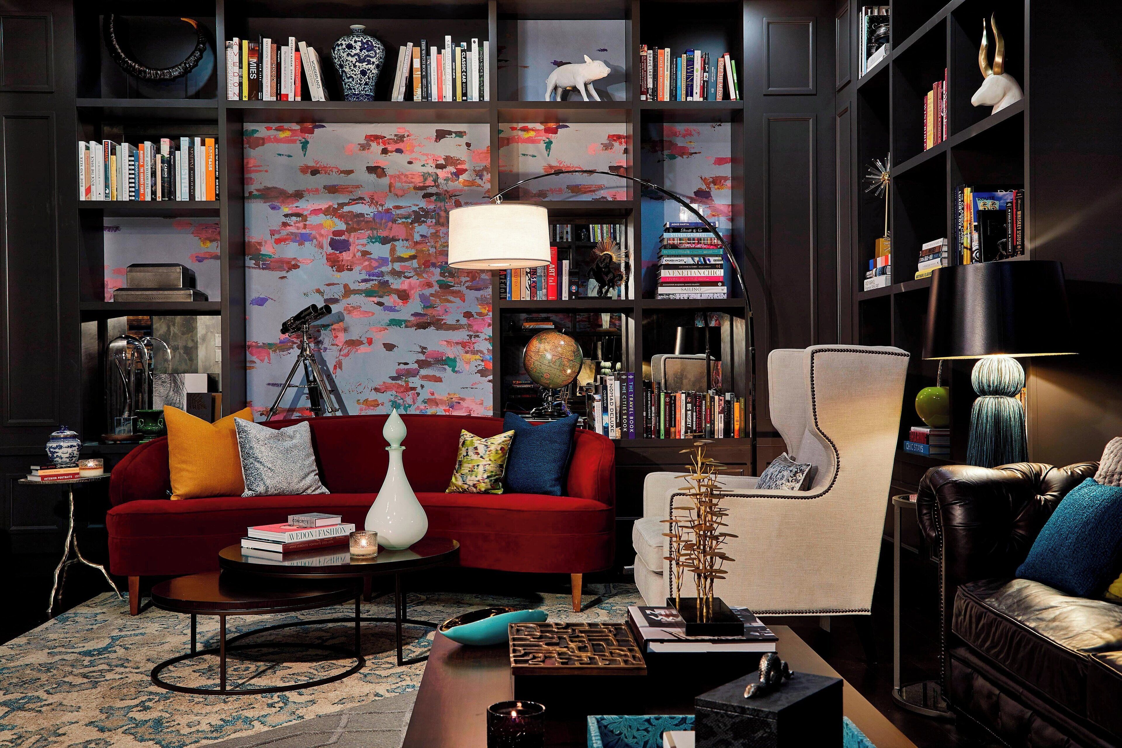 Una sala de estar moderna con un sofá rojo, un sillón blanco y una estantería llena de libros y objetos decorativos.