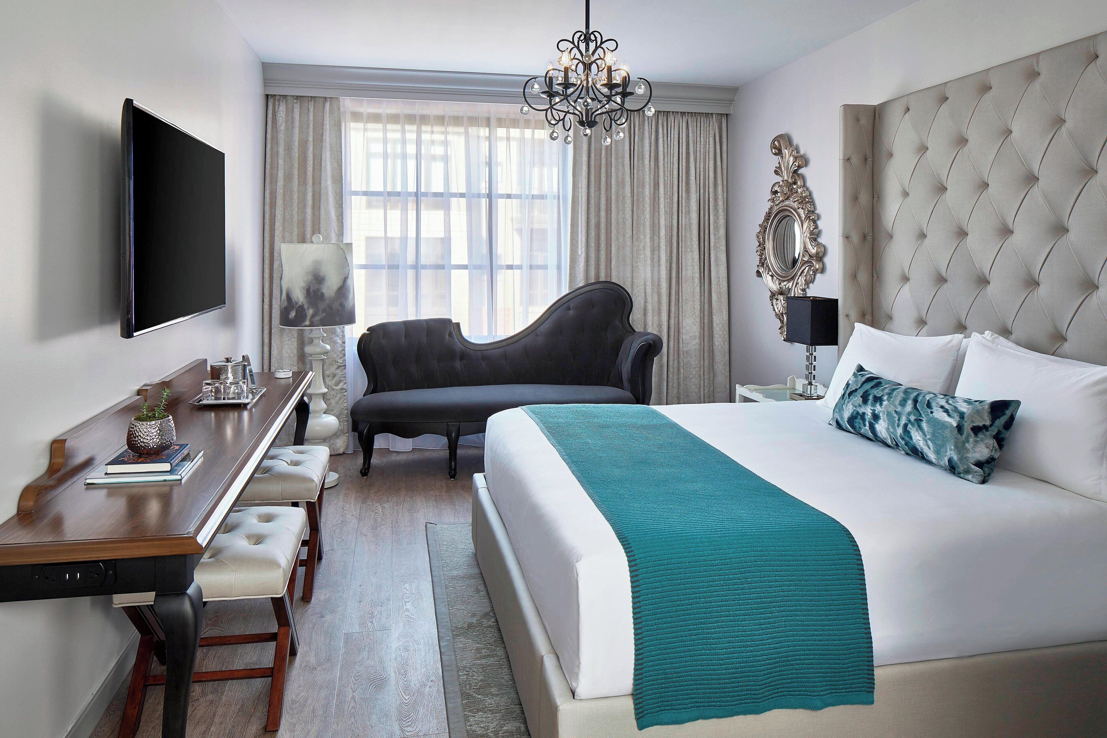 Une chambre d’hôtel avec un grand lit, un bureau avec une chaise, une télévision et un lustre.