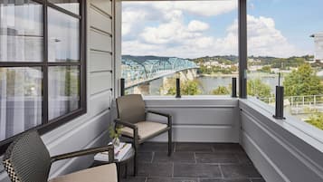 Ein Balkon mit Korbstühlen, einem kleinen Tisch und Blick auf eine Brücke über einem Fluss.