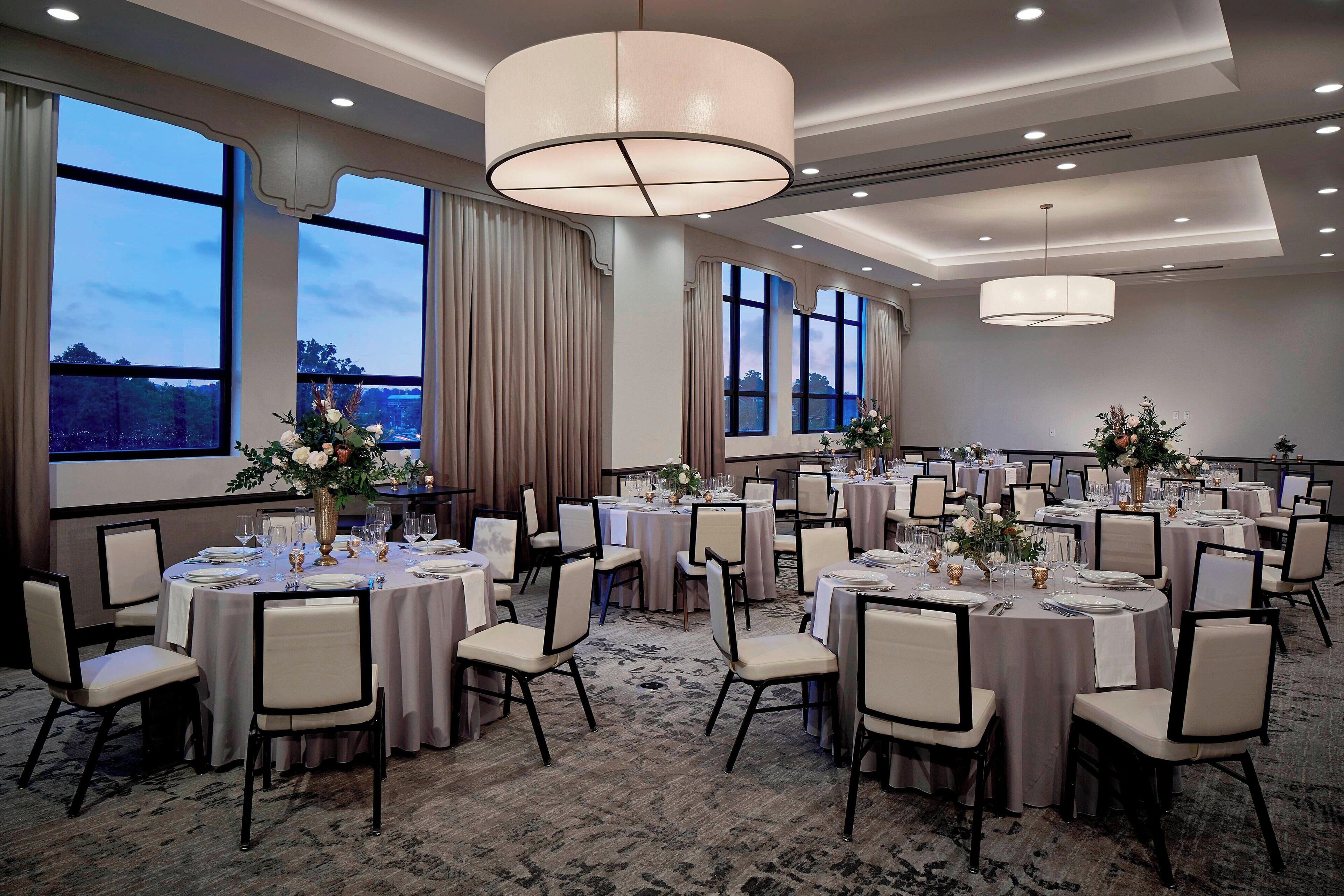 A banquet hall with round tables, chairs, and large windows.