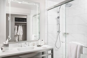 A modern bathroom with a large mirror, a glass shower enclosure, and a white sink with toiletries.
