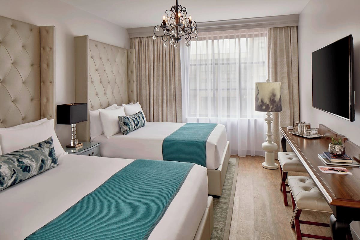 A hotel room with two beds, a chandelier, a TV, and a dining area with a table and chairs.