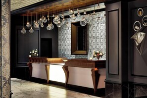 A modern hotel lobby with a reception desk, patterned wallpaper, and hanging crystal chandeliers.