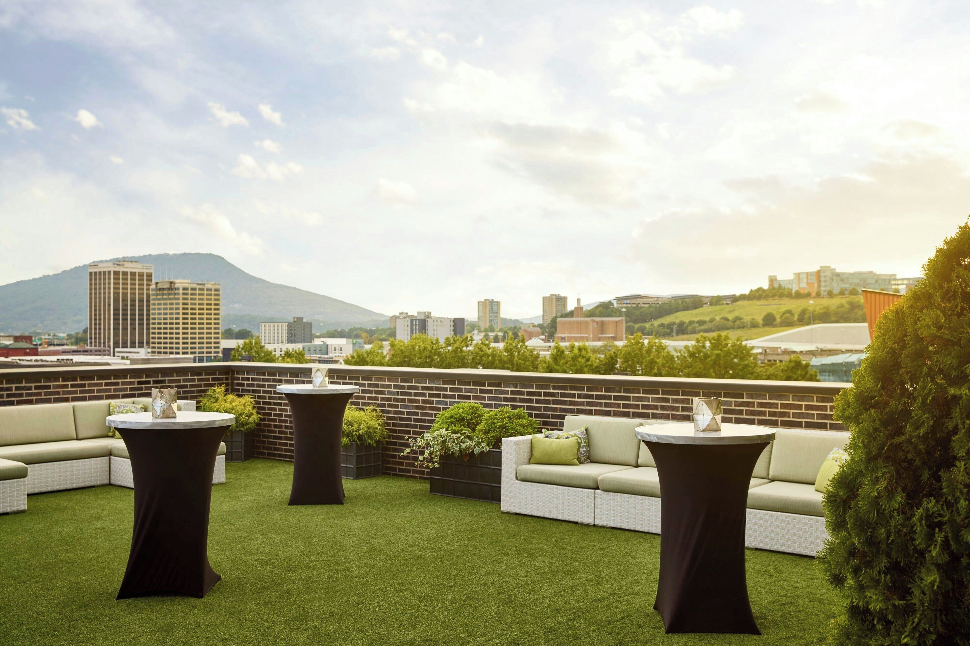 A rooftop terrace with artificial grass, two round tables, a sofa, and potted plants.