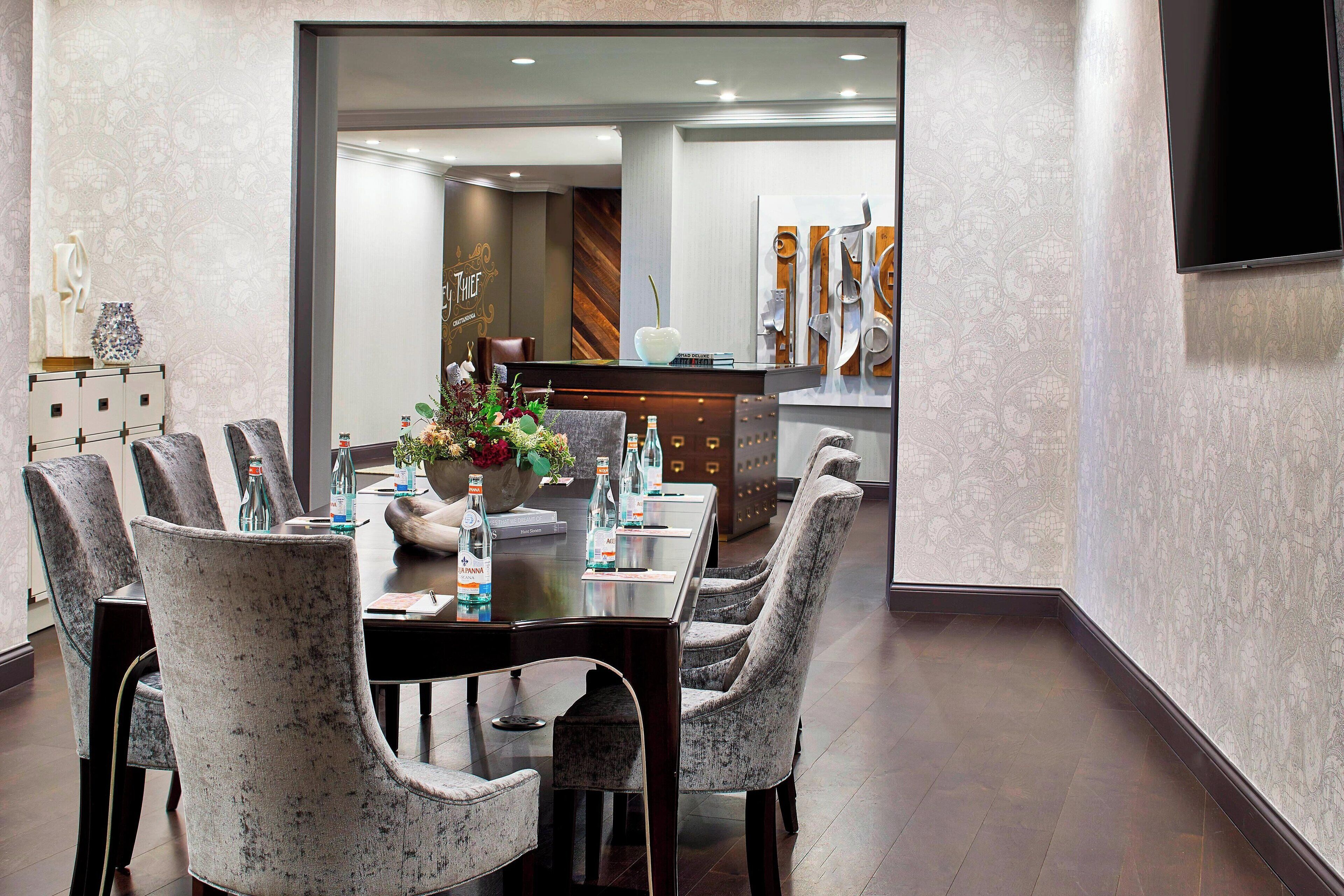 Un comedor moderno con una mesa larga, sillas grises tapizadas y un centro decorativo.