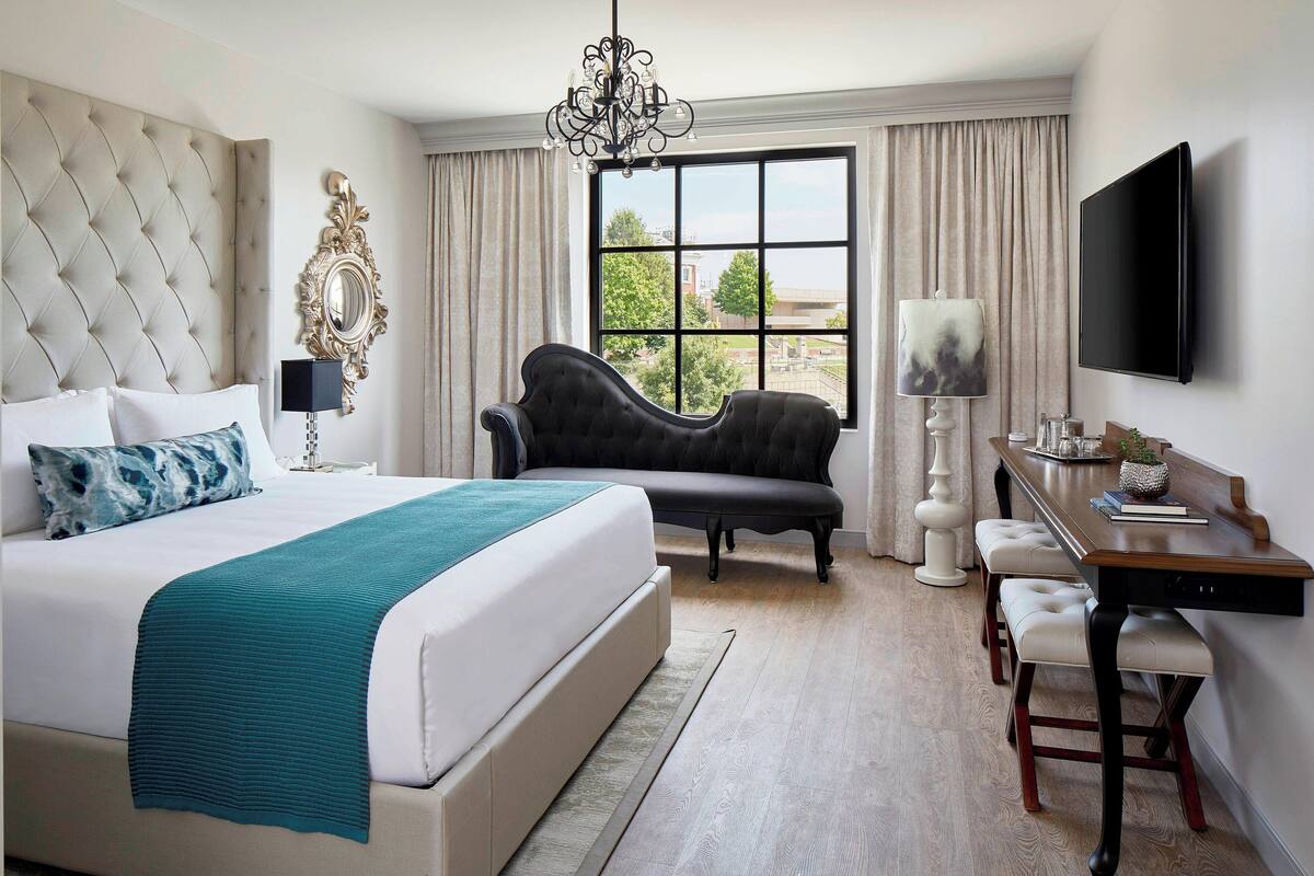 A hotel bedroom with a large bed, a chaise lounge, a desk, and a TV.