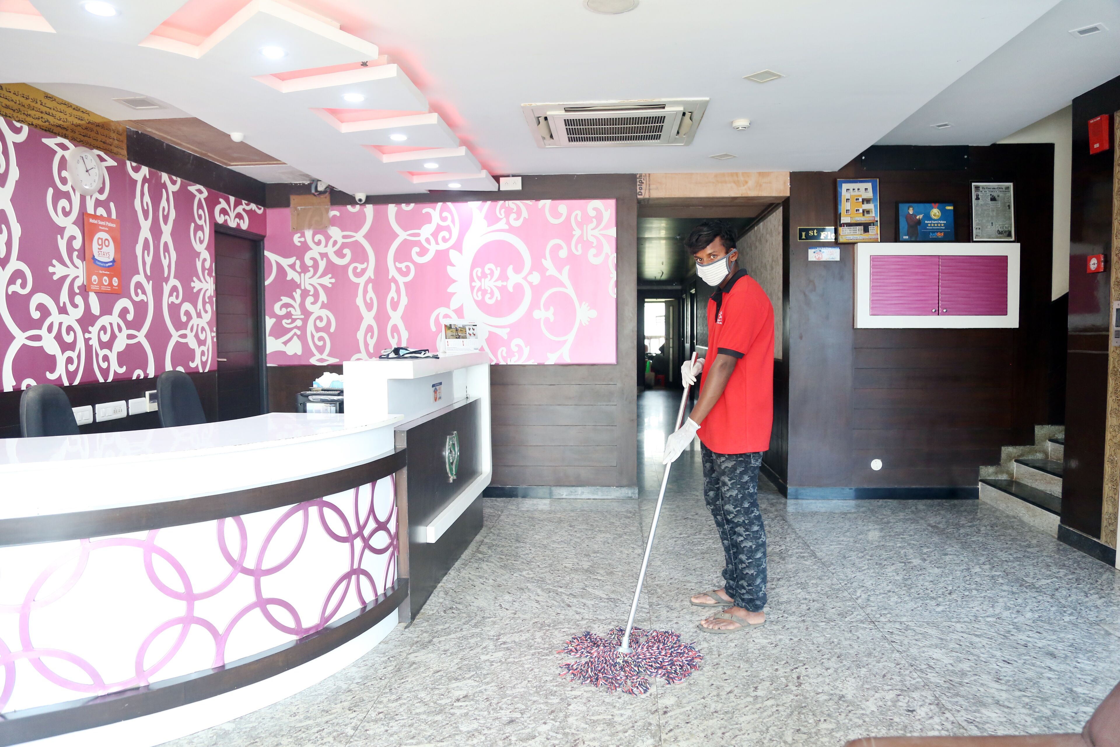 Zona de recepción de hotel con piso de mármol, un mostrador de recepción con fondo rosa y blanco estampado, y un hombre limpiando el piso.