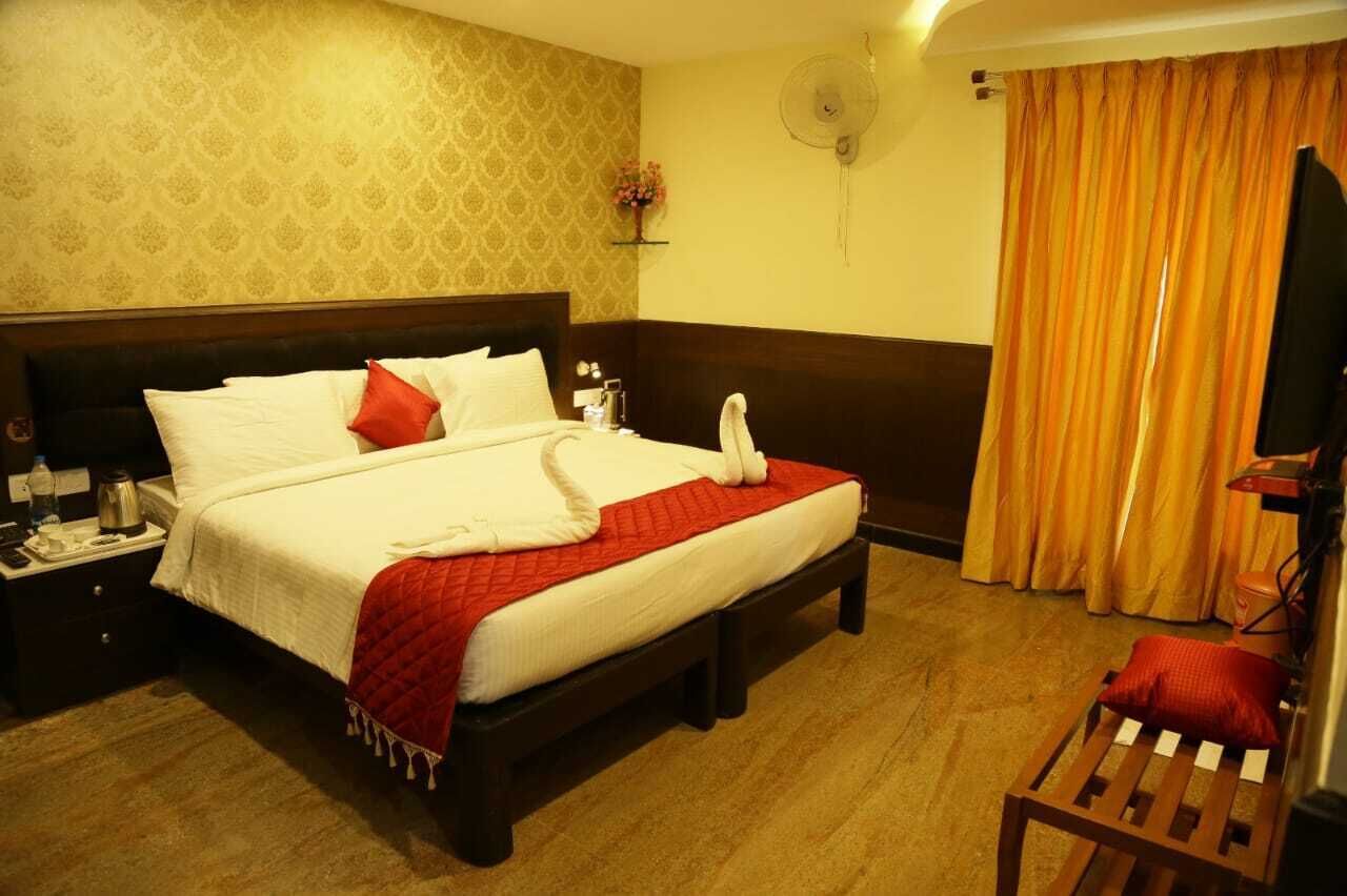Hotelkamer met een bed, nachtkastje, ventilator, televisie en raam met gordijnen.