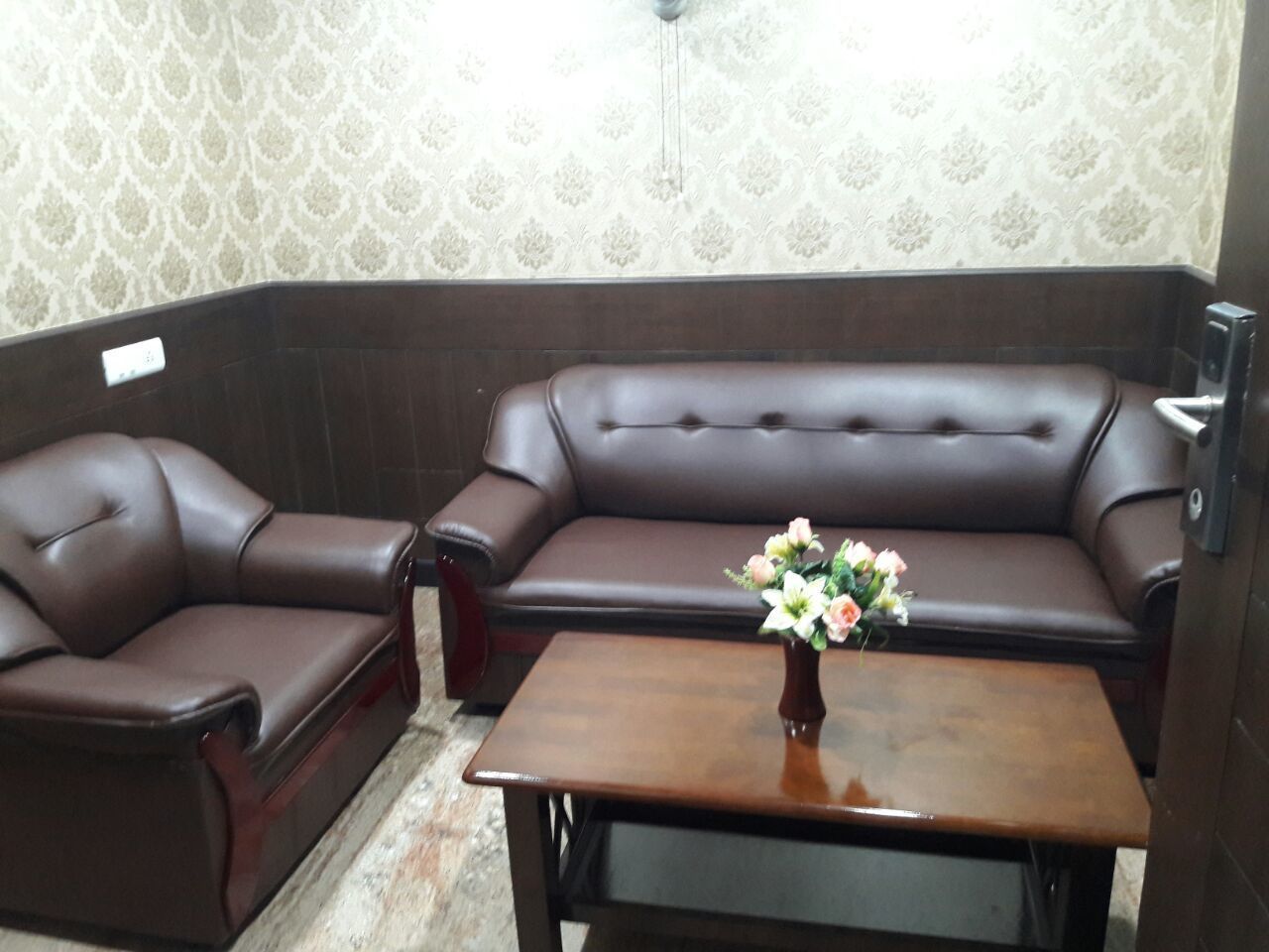 A brown leather sofa and armchair set with a wooden coffee table in a room with patterned wallpaper.