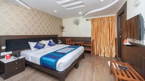 Une chambre d’hôtel avec un grand lit, un bureau, une chaise, une télévision et un ventilateur de plafond.