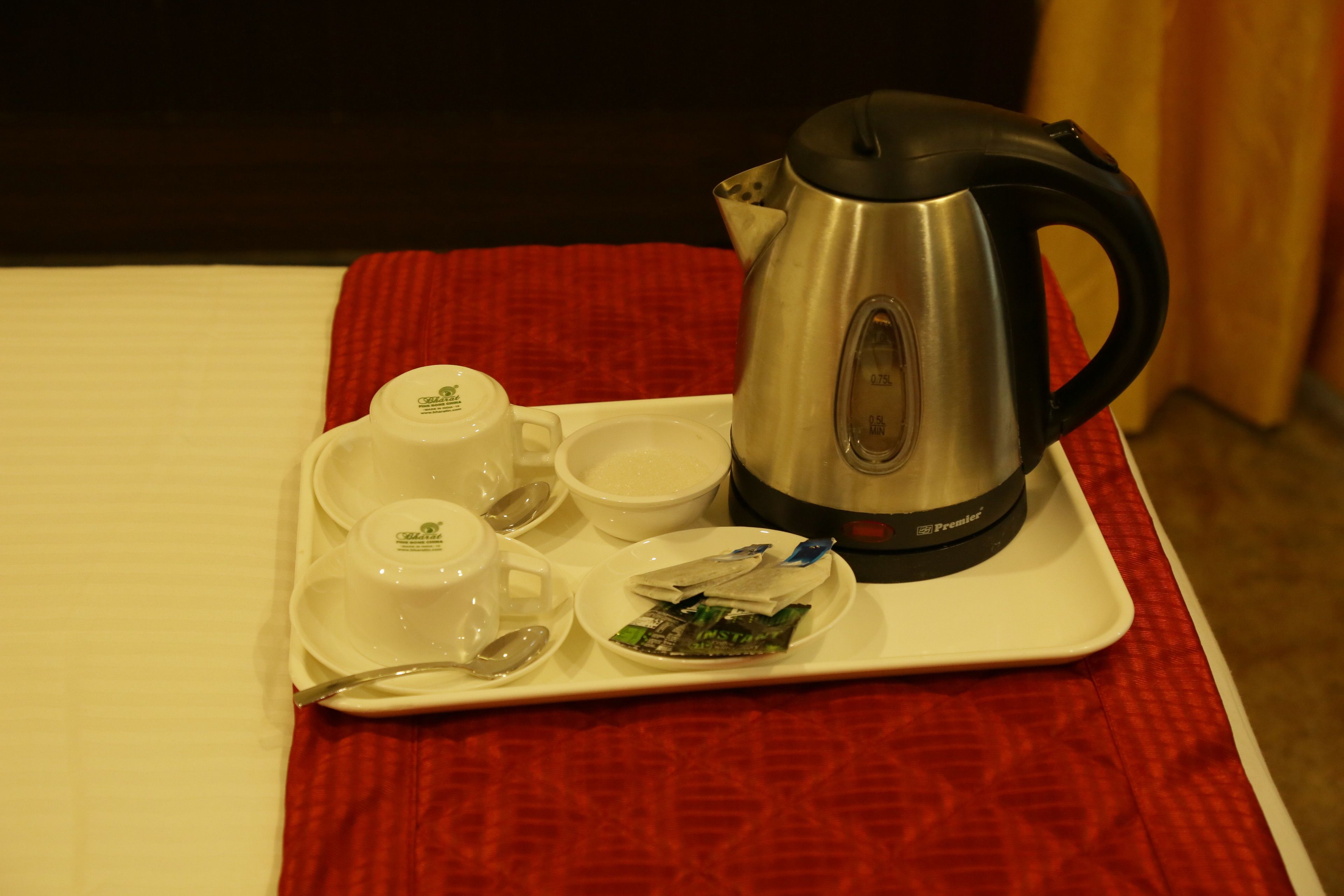 Una bandeja con una cafetera, tazas y un pequeño recipiente con bolsitas de té sobre una mesa con mantel rojo.