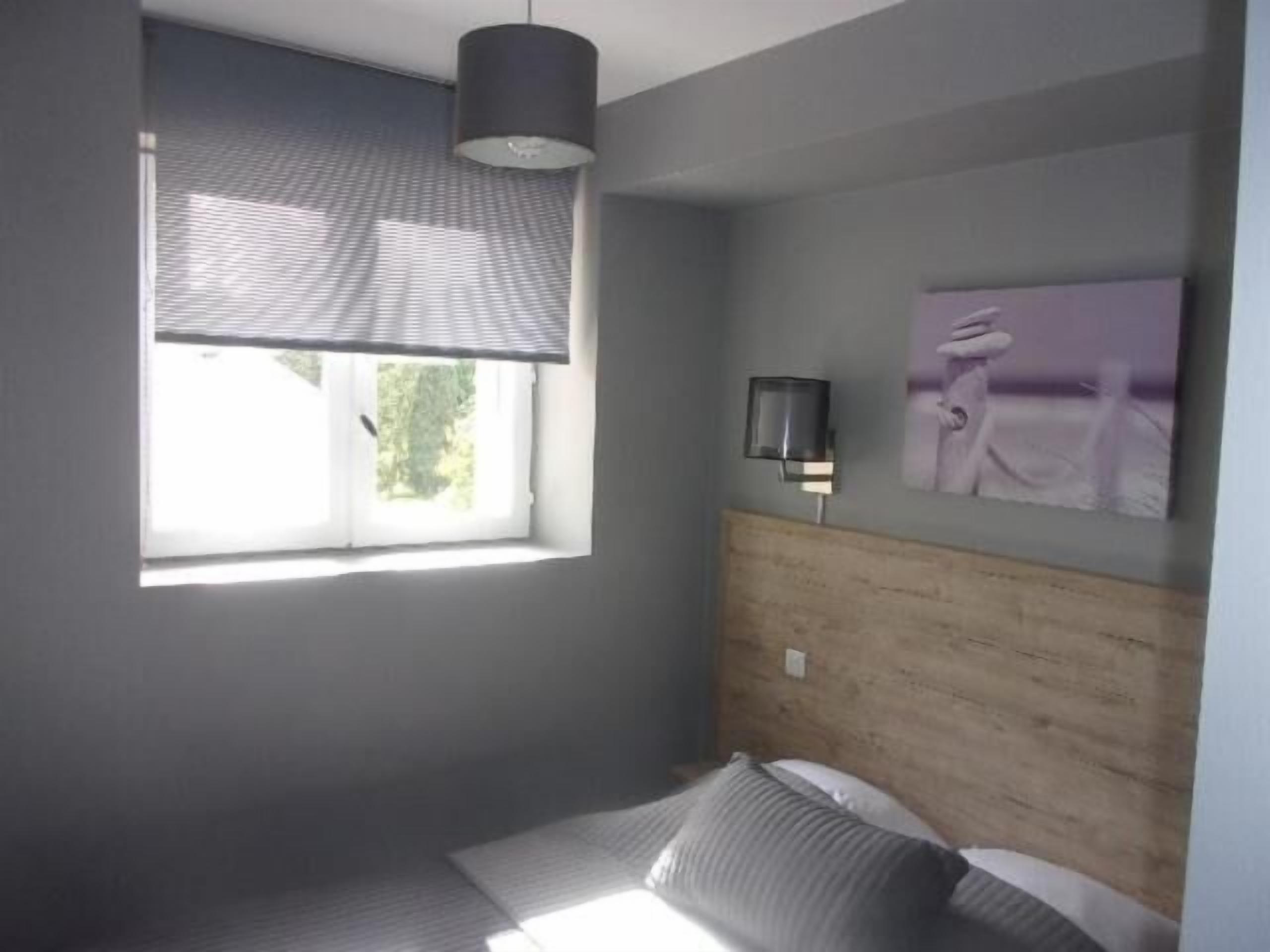 Ein Schlafzimmer mit Bett, einem Fenster mit Jalousien, einer Wandlampe und einem Gemälde.