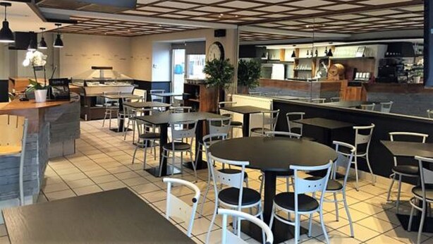 Un restaurante moderno con techo de diseño cuadriculado, varias mesas con sillas y una zona de cocina visible al fondo.