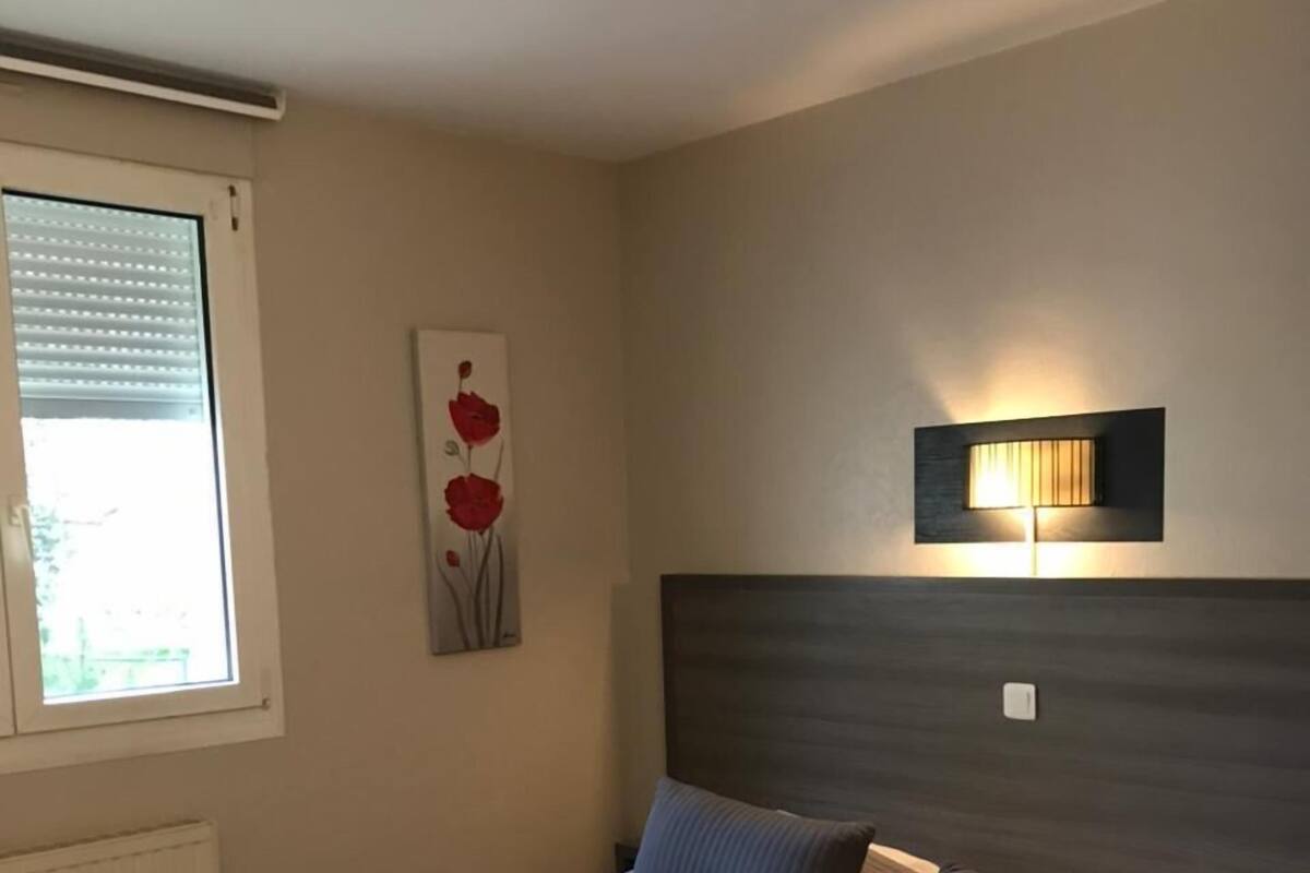 Une chambre à coucher comprenant un lit, une lampe fixée au mur, un radiateur et une fenêtre avec des stores.