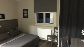 Un dormitorio con cama, escritorio, silla, ventana con persianas y radiador.