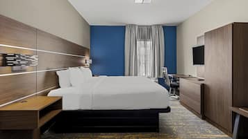 A modern hotel room with a large bed, wooden headboard, a desk, a chair, and a flat-screen TV.