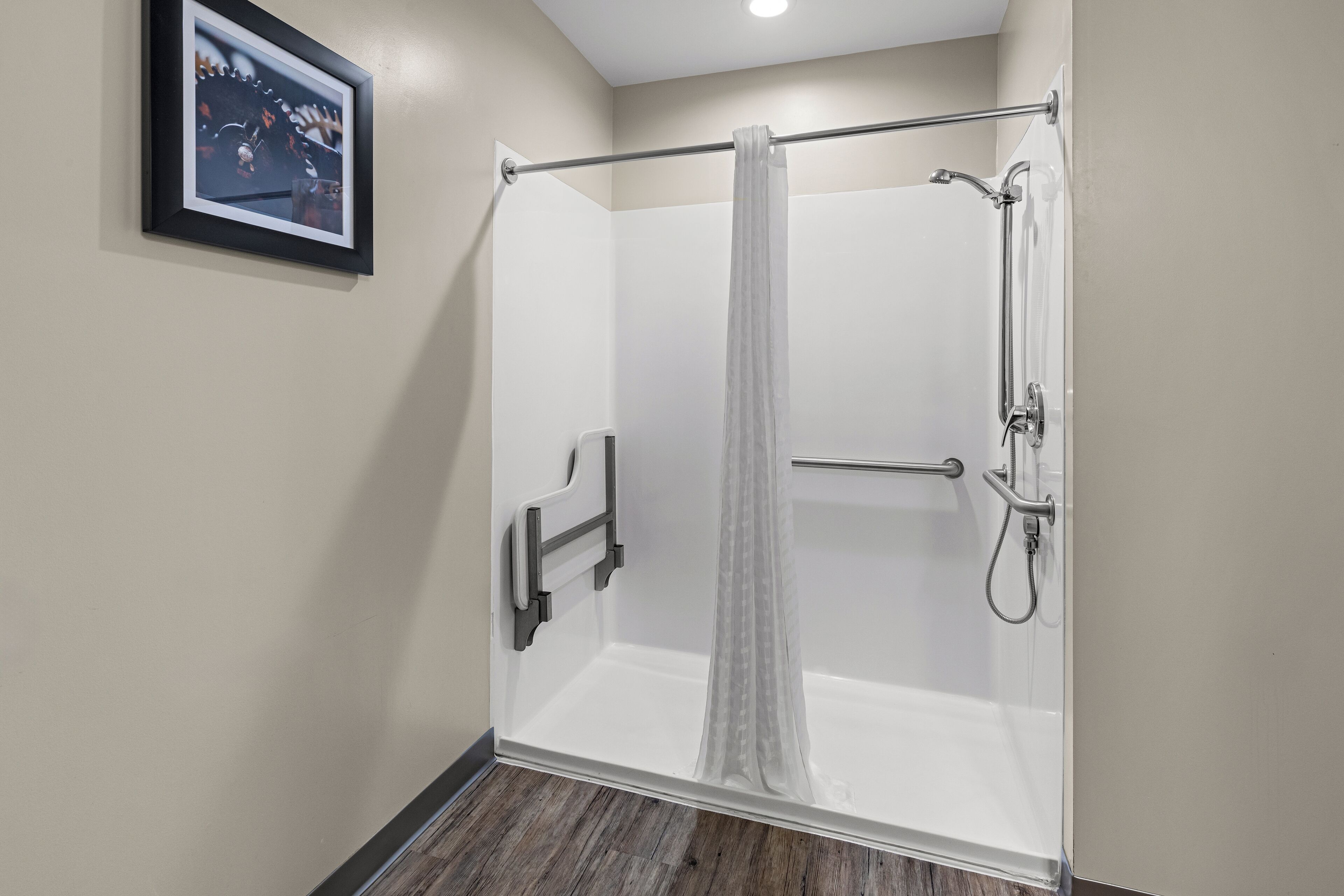 Une douche fermée par des parois en verre, avec un rideau blanc, une douchette à main et un robinet à main.