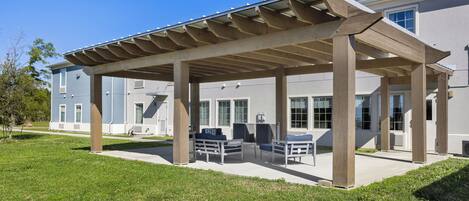 Un patio techado con mobiliario exterior, piso de concreto y un edificio al fondo.