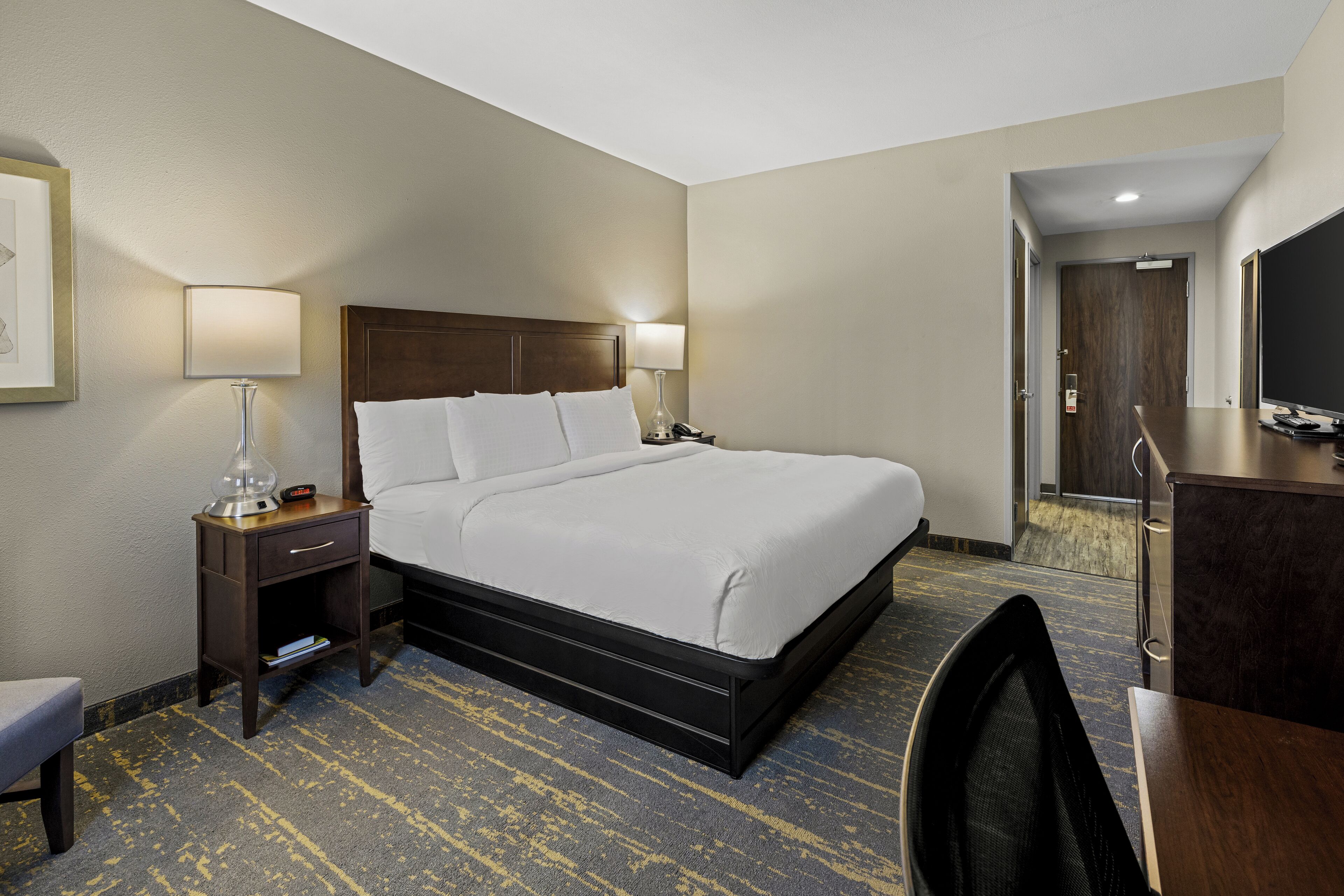 Une chambre d’hôtel avec un grand lit, deux tables de chevet avec des lampes, un bureau avec une chaise et un téléviseur.
