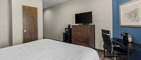 A hotel room with a large bed, a desk with a chair, a television, a coffee maker, and a framed artwork on the wall.