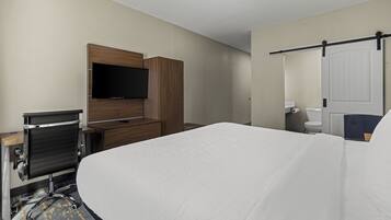Une chambre d’hôtel comprenant un lit, un bureau avec un ordinateur, un téléviseur fixé au mur, et une salle de bain avec des toilettes et un lavabo.