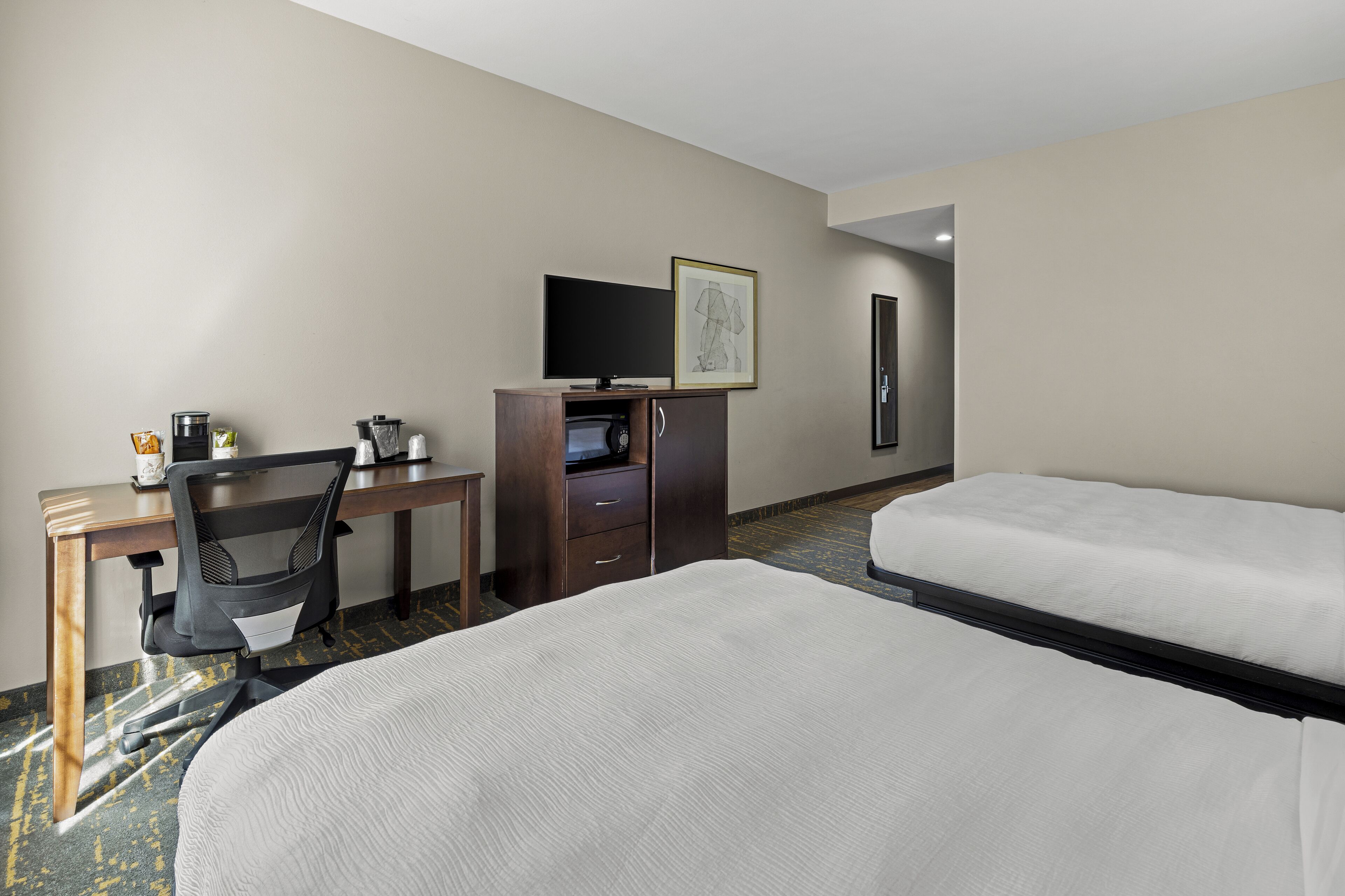 A hotel room with a bed, a desk with a chair, a television, a coffee maker, and a microwave.