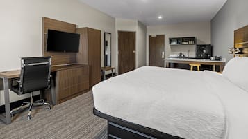 Habitación de hotel con cama, escritorio, silla, televisor, kitchenette y armario.