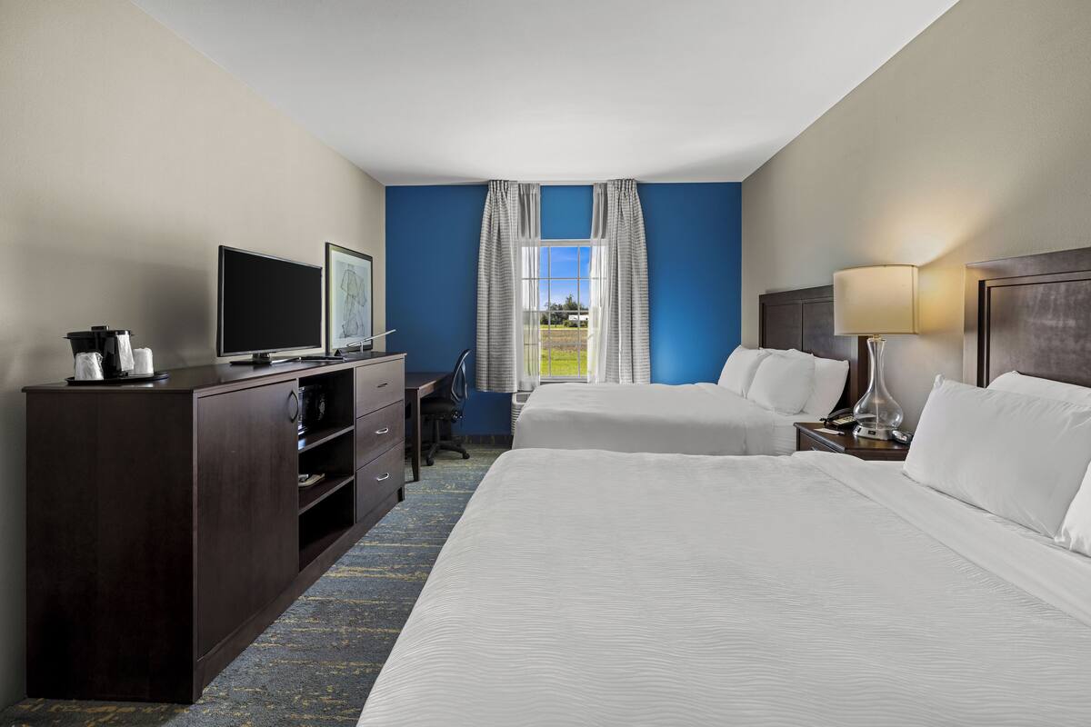A hotel room with two beds, a desk with a computer, a TV, and a window with curtains.