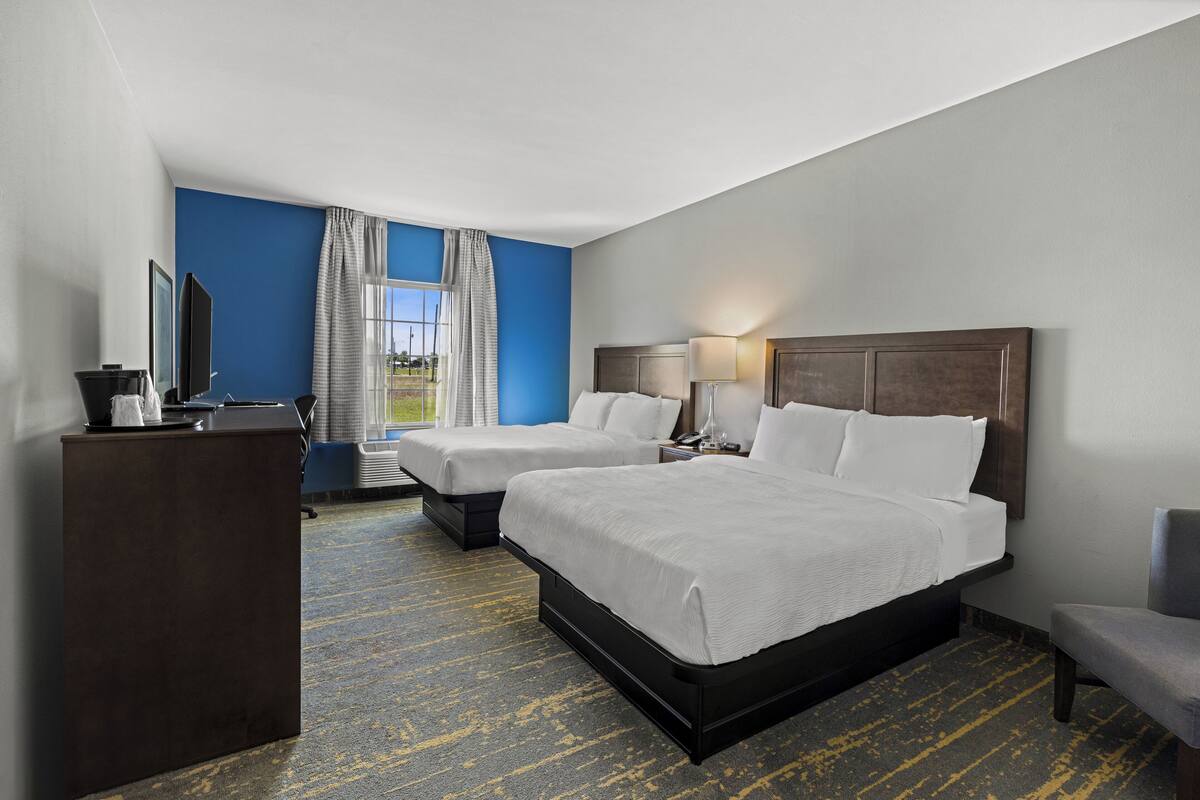 A hotel room with two beds, a desk, a chair, and a window with curtains.