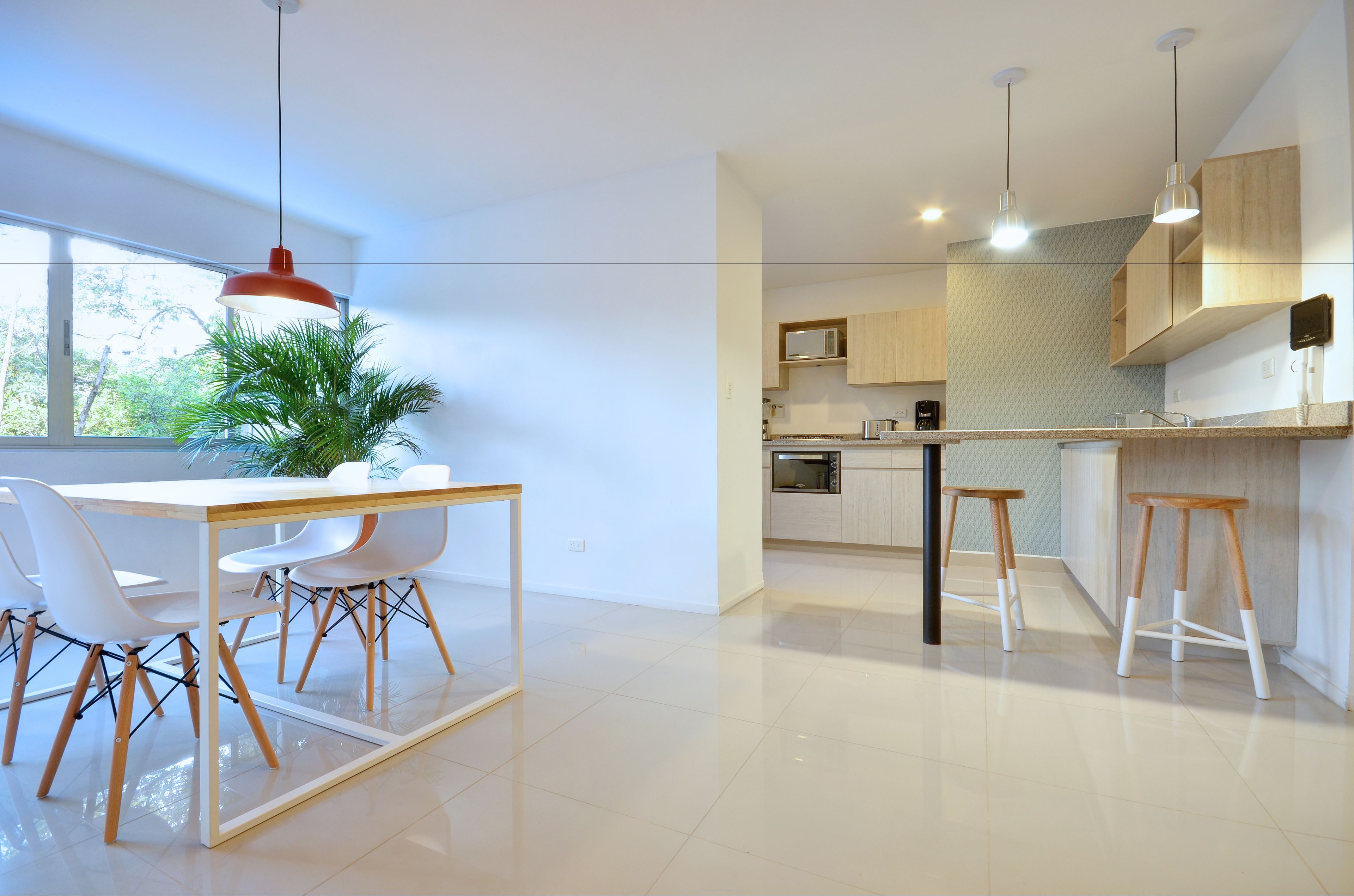 A modern kitchen with white cabinetry, a dining area with a white table and chairs, and a large window with a view of greenery.
