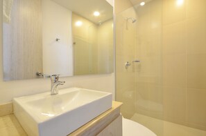 Un baño con lavamanos blanco, un espejo y una cabina de ducha de vidrio.