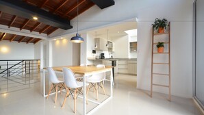 Une cuisine moderne avec des meubles blancs, une table à manger en bois et une étagère en forme d’échelle ornée de plantes.