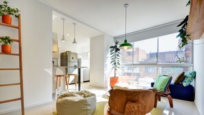 Un salon moderne avec un plancher en bois, un tapis à motifs verts, un fauteuil en forme de poire, une table basse en bois et un canapé bleu avec des coussins.