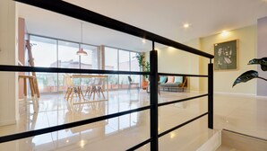 Un intérieur moderne avec une balustrade en verre, un coin repas comprenant des chaises et une table, et une grande fenêtre offrant une vue sur l’extérieur.