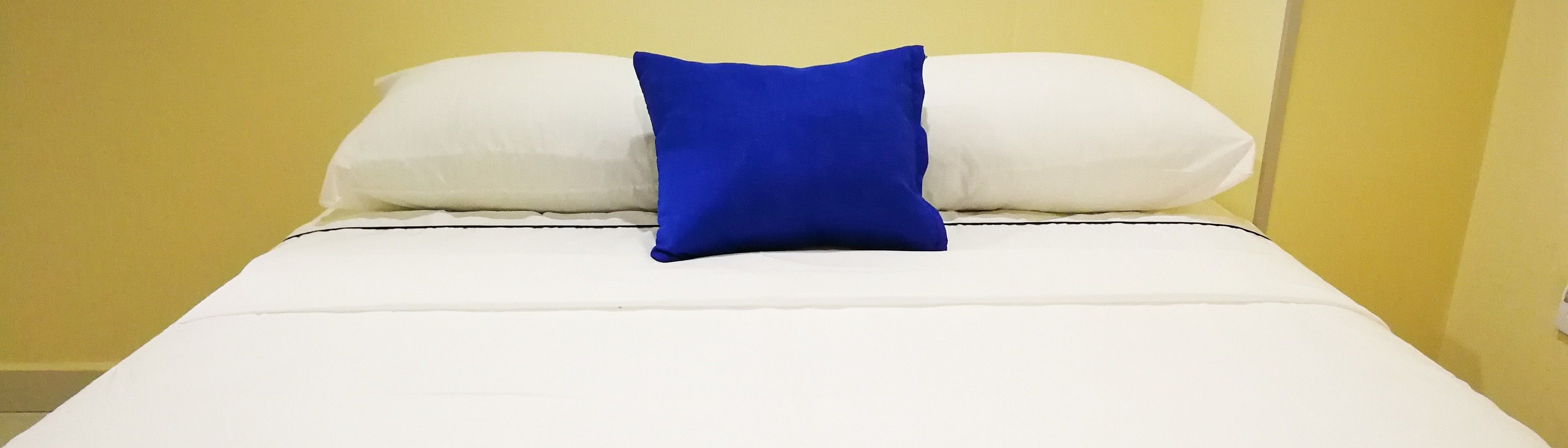 Un lit avec une literie blanche et un seul oreiller bleu.