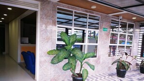 Un área de recepción con piso de mármol, plantas en macetas y un tapete de bienvenida azul.