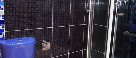A bathroom with a black tiled wall, a blue toilet, and a glass shower enclosure.