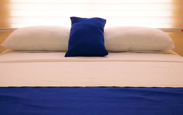 Una cama con un almohadón azul y dos almohadones blancos.