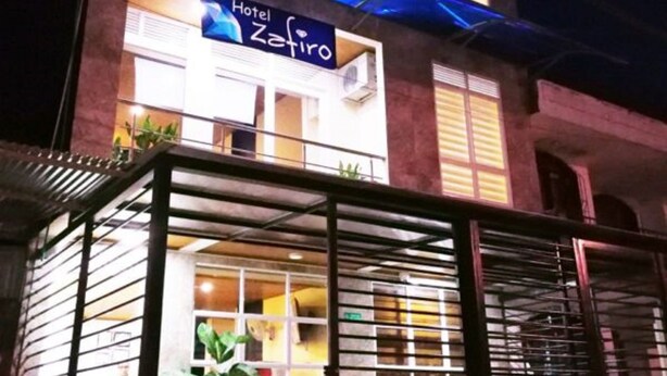 Un hotel llamado "Hotel Zafiro" con fachada moderna, ventanas amplias y un área de entrada cubierta con plantas en macetas.