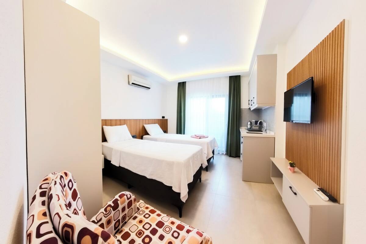 A hotel room with two beds, a TV, a small kitchenette, and a seating area.