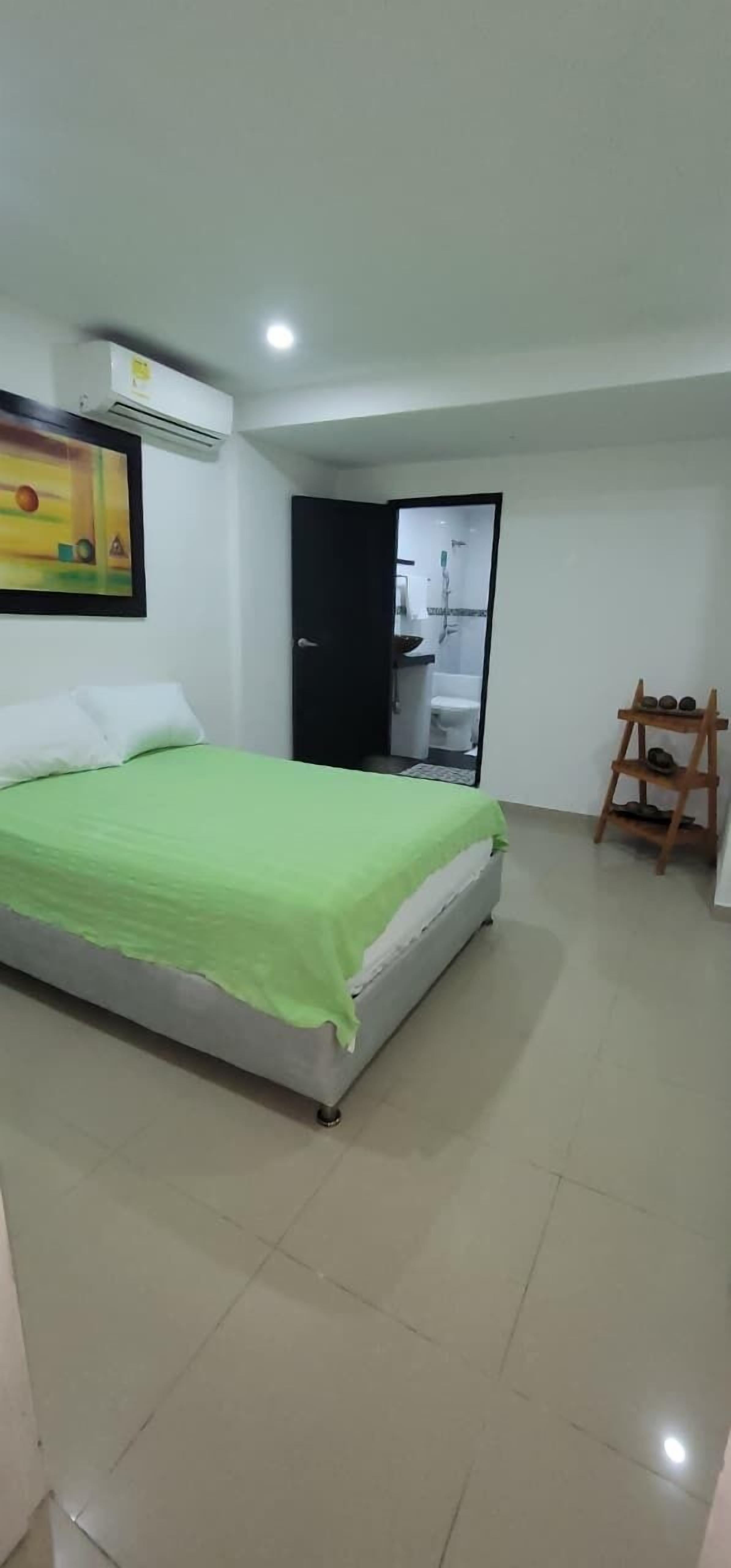 Une chambre à coucher avec un lit, une porte donnant sur une salle de bain et une petite étagère en bois.