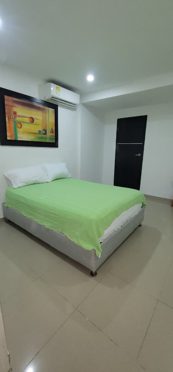 Una habitación con una cama, un cuadro en la pared, un equipo de aire acondicionado y una puerta.