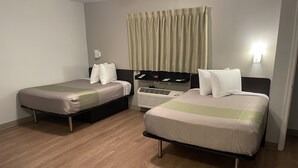 A hotel room with two single beds, a bedside table with a lamp, a wall-mounted air conditioner, and a window with curtains. - Studio 6 Extended Stay - Richmond, VA - I-64 West (Richmond)