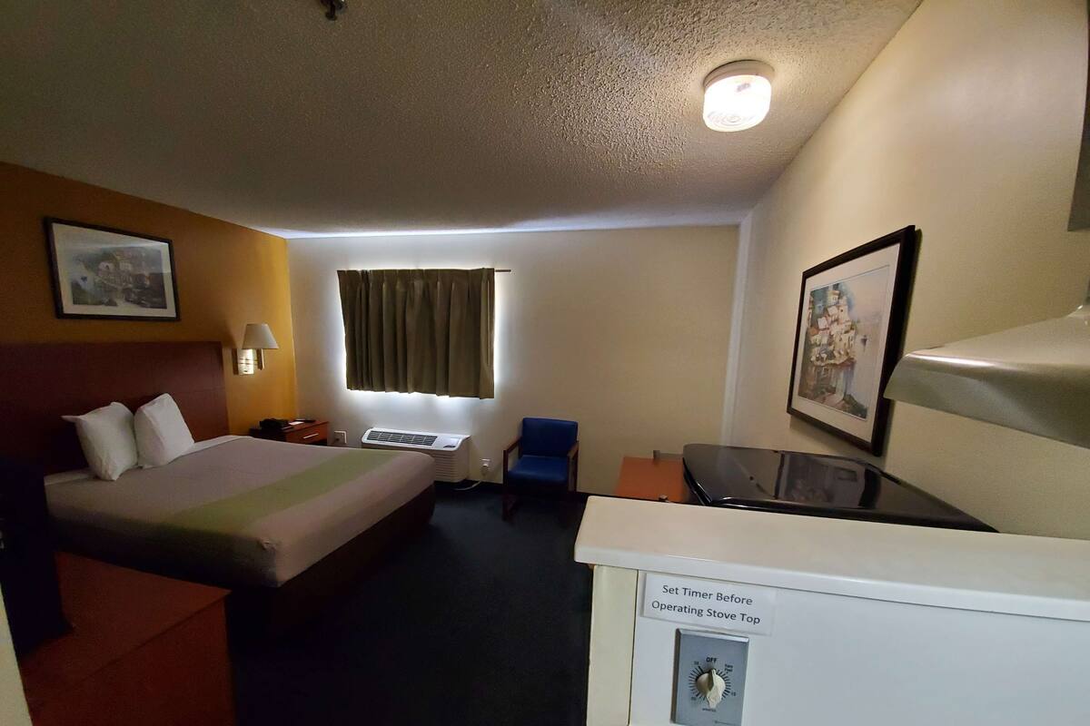 A hotel room with a bed, a desk, a chair, a heater, and a wall-mounted air conditioner.