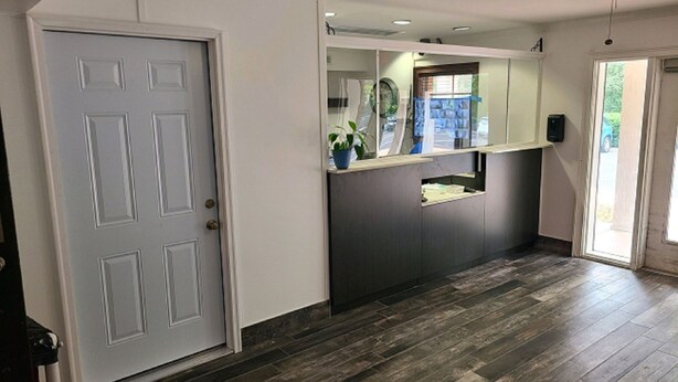 A hallway with a grey door, a reception desk, and a ceiling fan. - Studio 6 Extended Stay - Richmond, VA - I-64 West (Richmond)