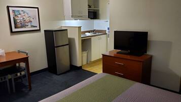A compact hotel room with a bed, a small desk, a refrigerator, a television, a microwave, and a kitchenette.