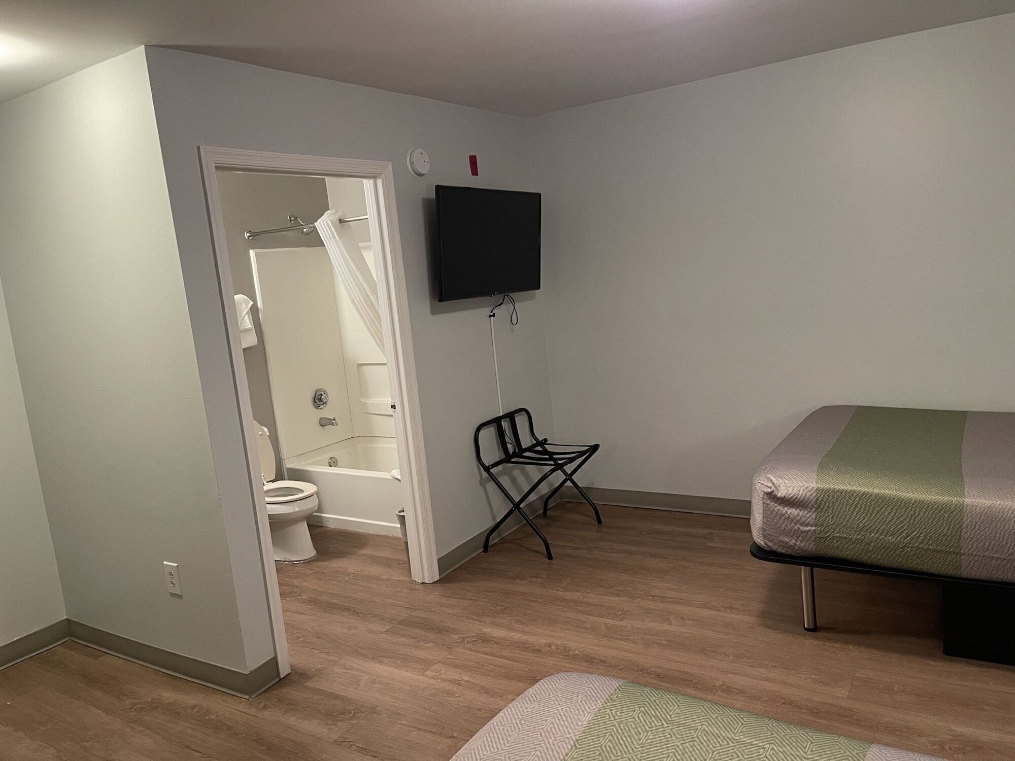 A bedroom with a bed, a TV, a chair, and a bathroom visible through an open door.