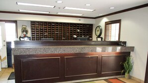 A reception area with a check-in counter, a clock, and a patterned carpet. - Studio 6 Extended Stay - Richmond, VA - I-64 West (Richmond)