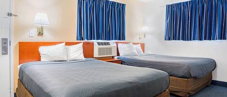 A hotel room with two beds, a wooden headboard, a wall-mounted air conditioner, and blue curtains.